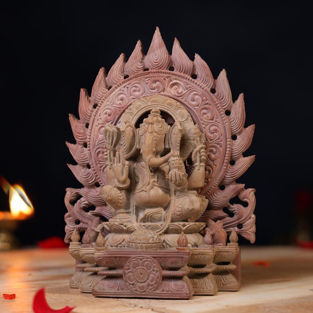 Handcrafted Ganesh idol in pink stone seated on throne with visible intricate carvings on the side
