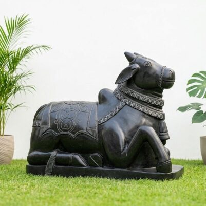 Front view of a black stone statue resting on a grassy surface, featuring a handcrafted Nandi idol.